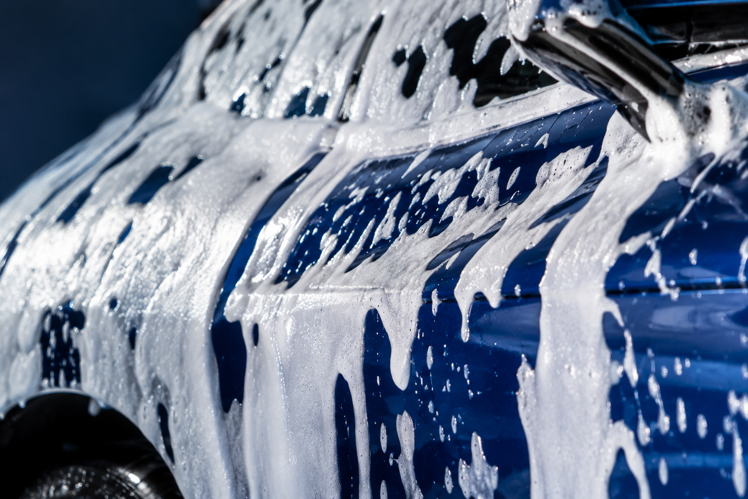 Thick snow foam dripping down blue vehicle paintwork
